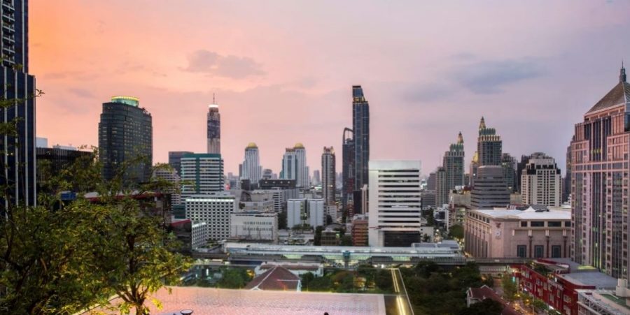 A panoramic city skyline at sunset, featuring darkened buildings set against a dramatic, colorful sky.